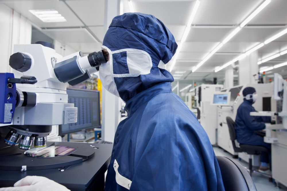 Reinraum, Person mit blauem Reinraumanzug sitzend am Mikroskop / Cleanroom, person with blue cleanroom suit sitting at the microscope