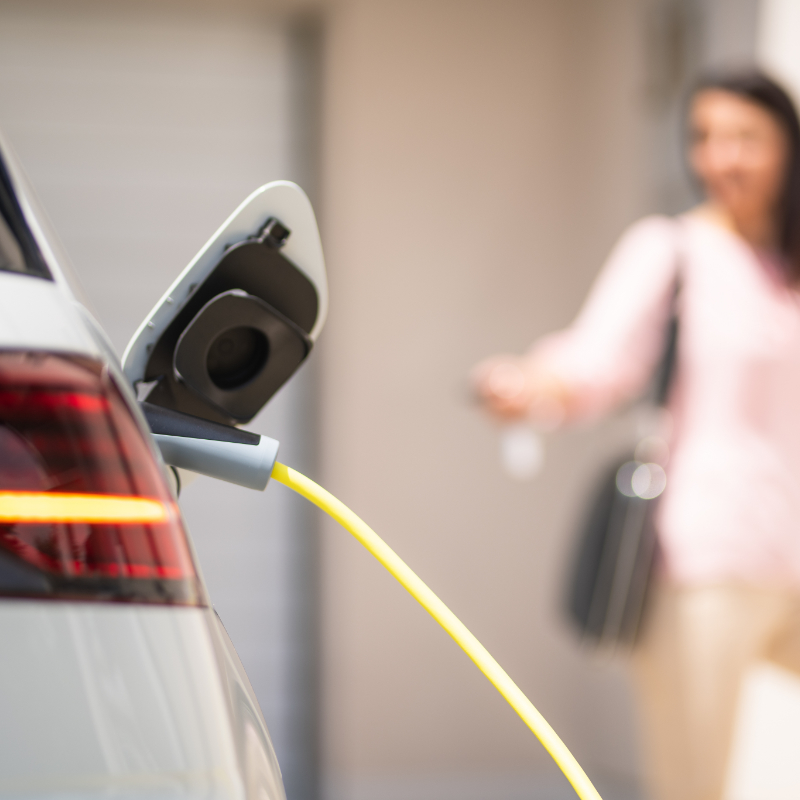 Close up of a electric car charger with female silhouette in the background, entering the home door and locking car